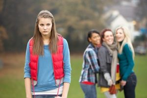 A picture of a single female teen walking away from a group bullying her. This illustrates what can happen without the benefit of teen self defense classes